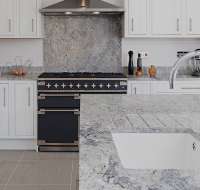 Kitchen with grey granite worktops featuring a large island, white ceramic sink, chrome hardware, and matching granite upstands and splashback.
