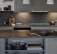 Modern kitchen with dark granite worktops and matching full height upstands with grey units.